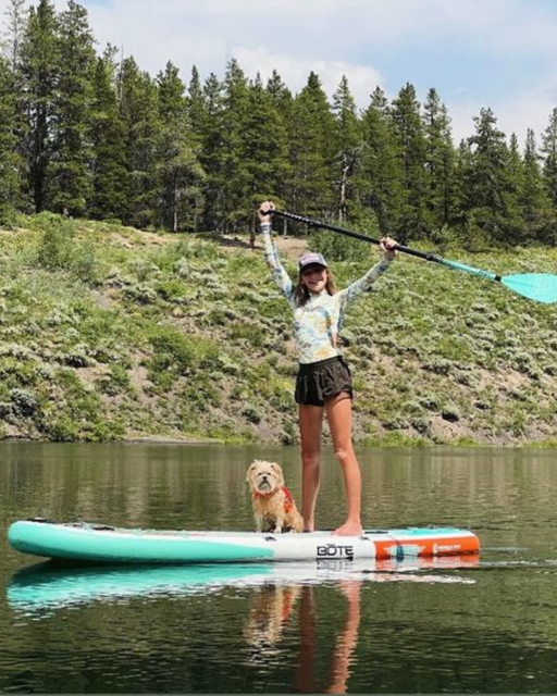 Woman paddle boards in the water with her small dog