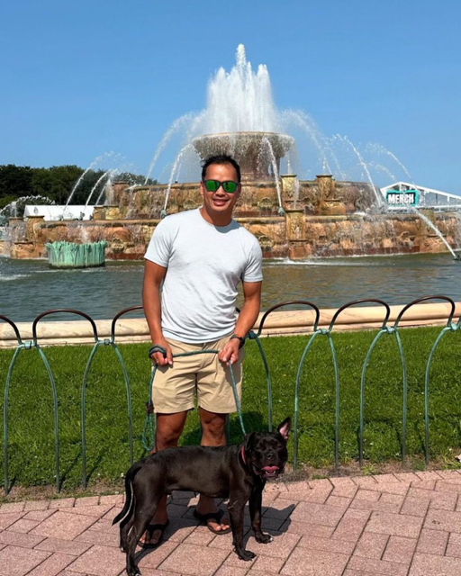 Man and his Boston terrier stand in front of a fountain