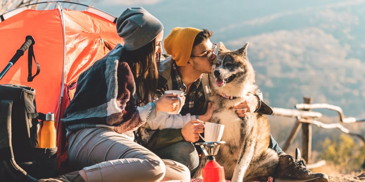Couple drinking from mugs outside their tent with a large dog