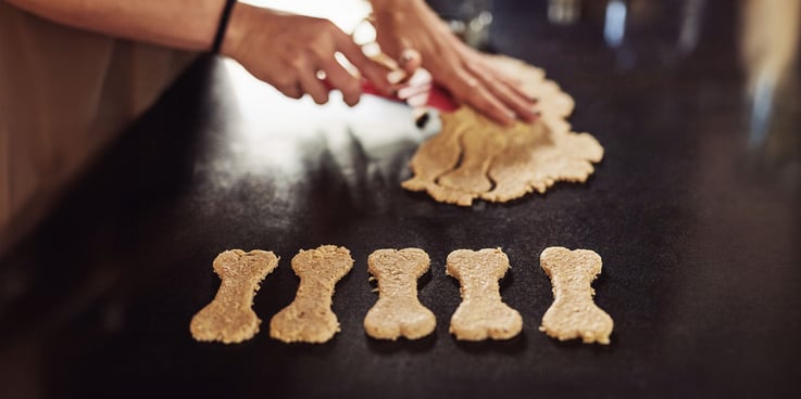 Hands cut bone-shaped cookies from a wad of cookie dough