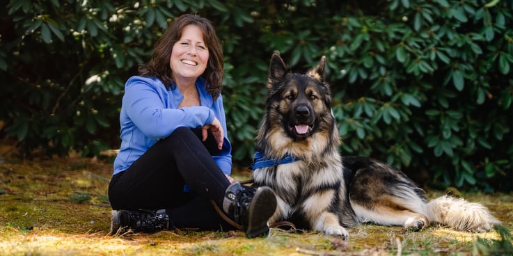 a woman in hiking gear sits beside her shiloh shepherd dog outside