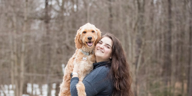 Woman stands in a snowy backdrop with large goldendoodle in her arms