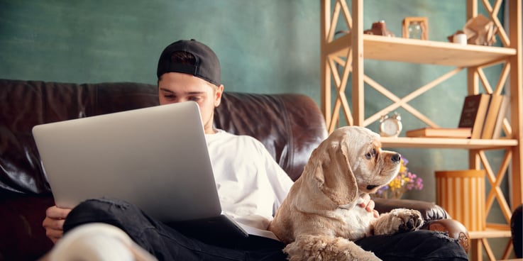 Young man sitting on the couch with his laptop and his dog