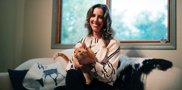 Dr. Emily Tincher sits on a sofa with her orange cat, Exploding PopTart