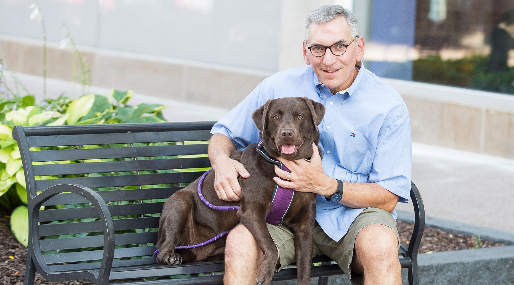 Member Tim P. sits on a bench with Labrador retriever Maeve in his lap