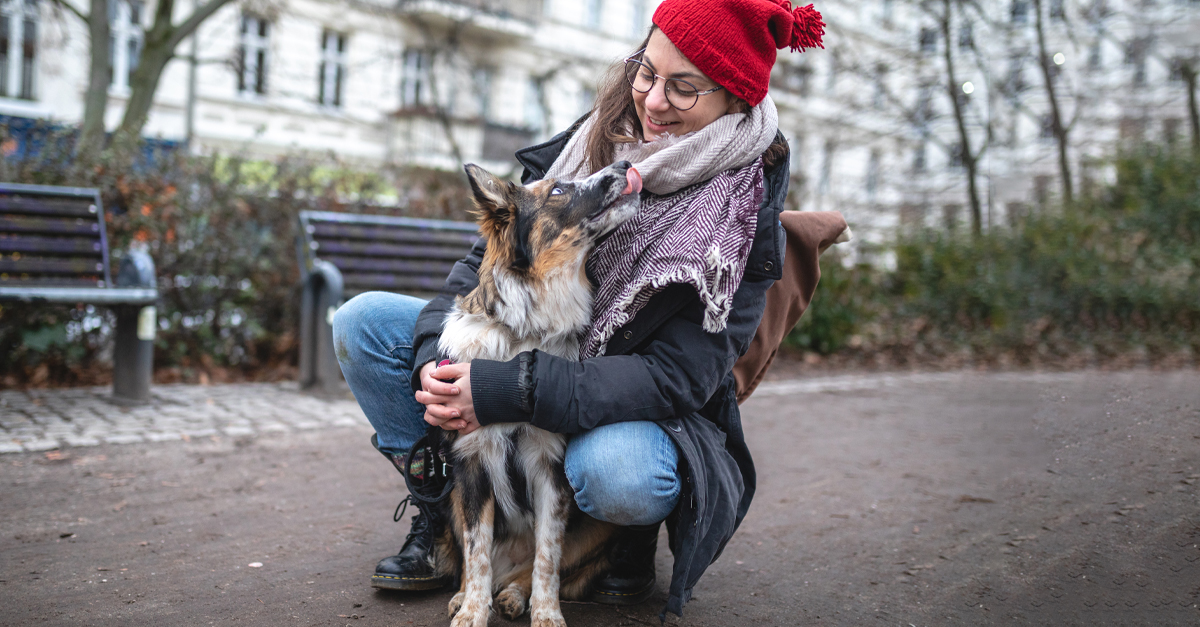 Woman in red beanie smiling while holding medium sized dog